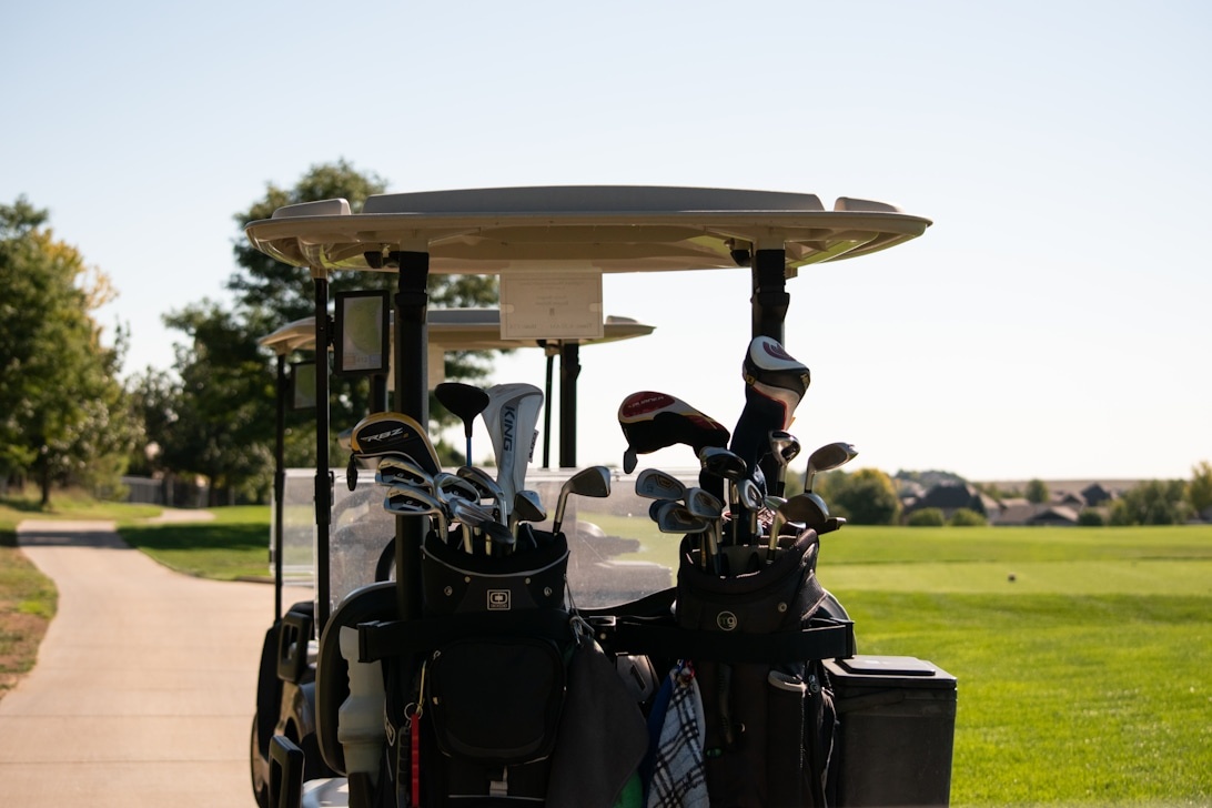Une voiturette de golf avec deux sacs de golf complets à l'arrière, garée sur le chemin d'un parcours.