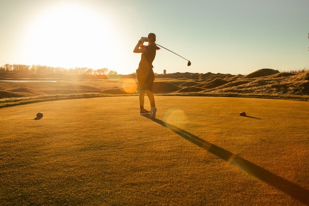 Golfeur terminant son geste sur le green au soleil couchant